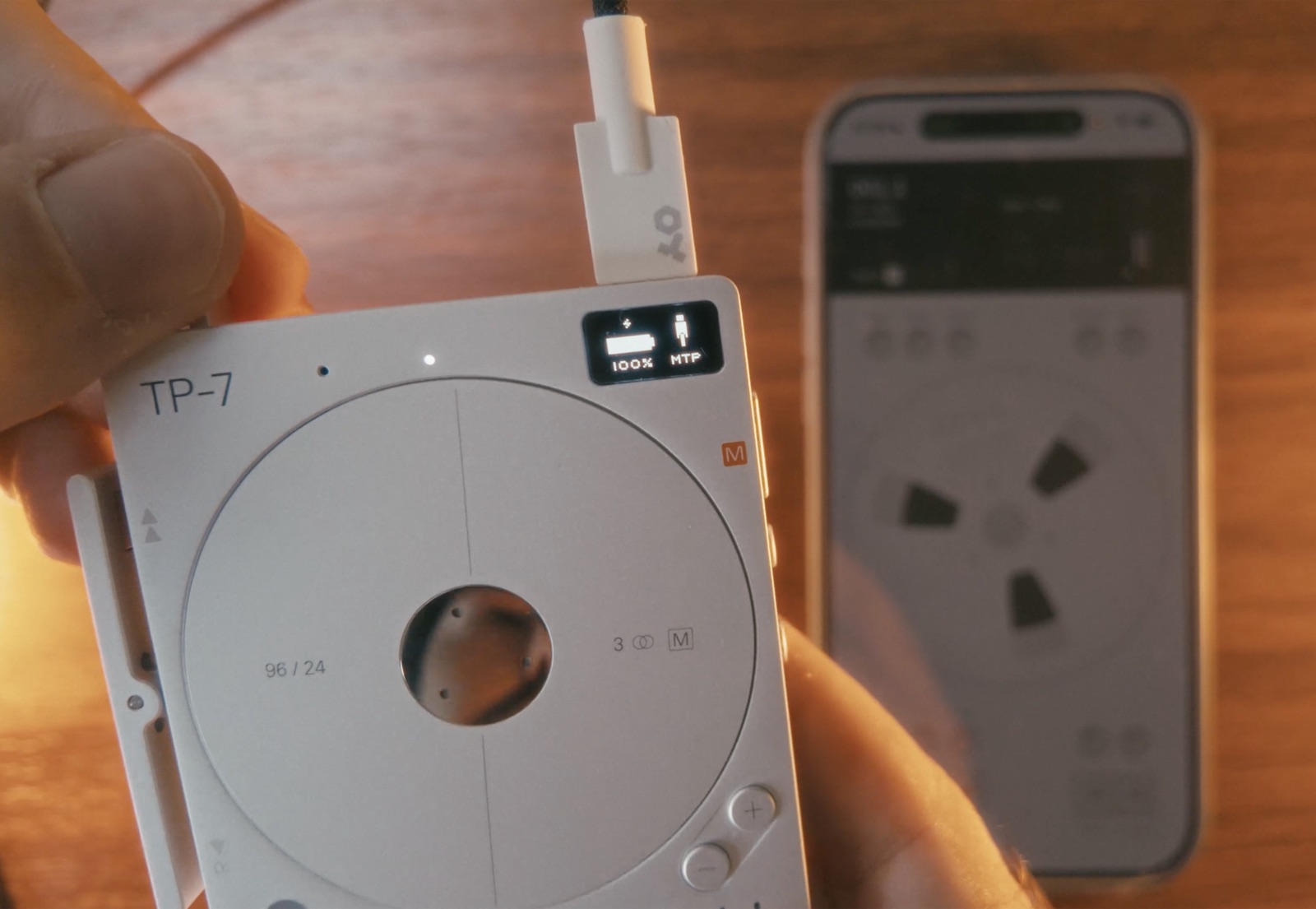 A Teenage Engineering TP-7 connected to an iPhone by a single USB-C cable, the TP-7's own display reading MTP, with Reel open on the phone